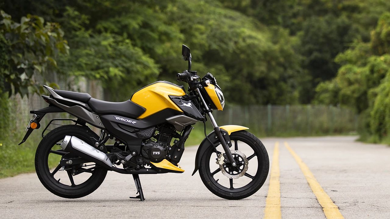 TVS Rider 125 in yellow and black color on road near tress