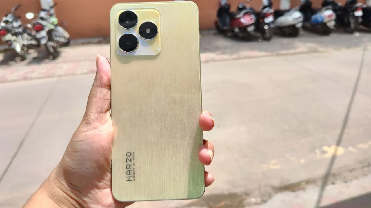 Realme Narzo N53 in gold color in a hand near road and bikes