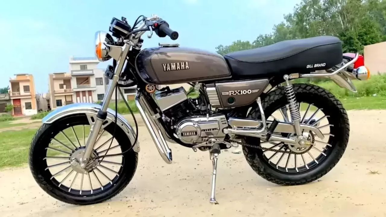 Yamaha RX 100 in brown and black color near grass infront of some buildings