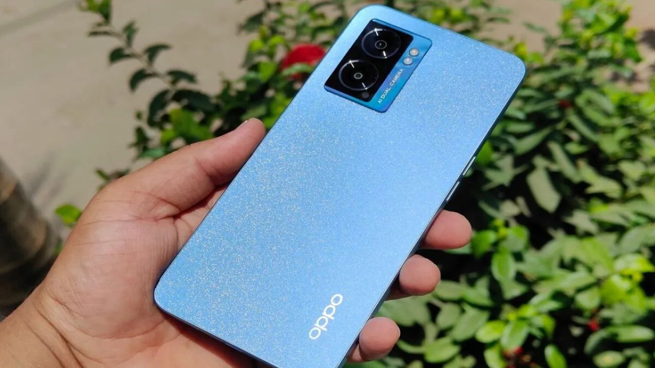 oppo k10 5g in blue color in a man hand infront some flower plants